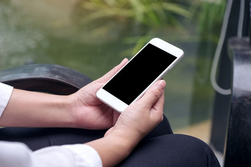 Mockup image of a woman holding white smart phone with blank black desktop screen with blur green nature background