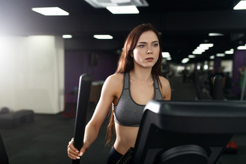 Fototapeta na wymiar Attractive fitness girl doing exercise on machine treadmill. Pretty girl doing workout at modern fitness gym.