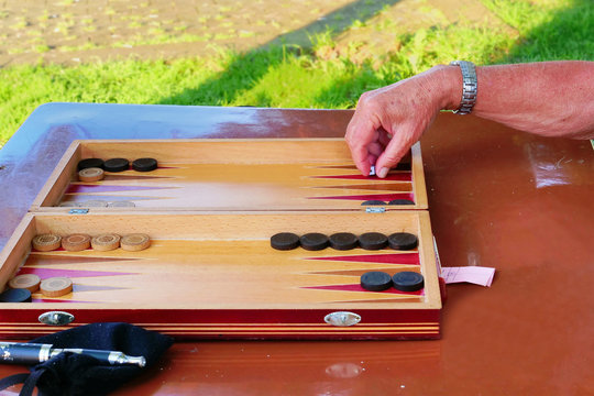 Senior male hand rolls the dice playing backgammon game at an outdoor table