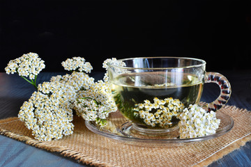 Yarrow medicinal tea in glass cup and yarrow flowers on wooden table over dark background (Achillea millefolium)
