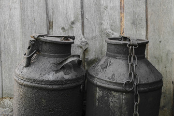 Black and oiled metal canisters in the countryside. Wooden wall in background