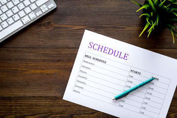 College or school schedule with lessons and bell time. Student planner on dark wooden work desk with computer and pen top view space for text