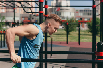 Fototapeta na wymiar A young man on the Playground doing exercises on the bars
