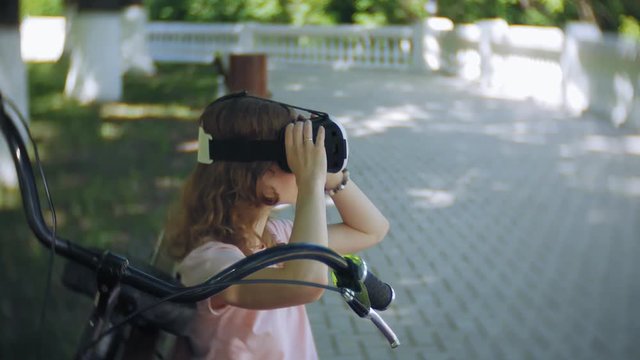 Young woman uses head-mounted display in the park. Playing game using VR-helmet for smart phones. Happy