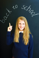 Happy little  school girl near school blackboard