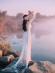 A river nymph in a white lace dress stands on a rock by the lake. The princess has a beautiful...