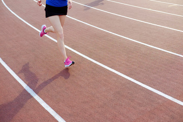 Fototapeta premium Athletic young woman in pink sneakers run on running track stadium
