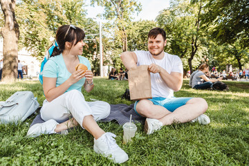 couple sitting on green grass eating burgers drinking smoothie