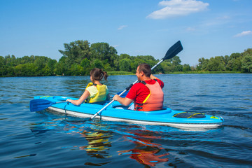 Young couple kayaking down the river in a blue kayak on a beautiful sunny day