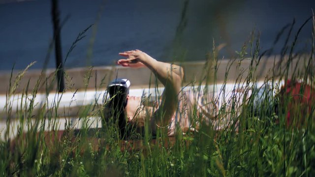 Young woman uses head-mounted display in the park. Playing game using VR-helmet for smart phones. Happy