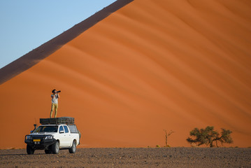 Young Asian man traveler and photographer standing on camper car near orange sand dune. Travel...