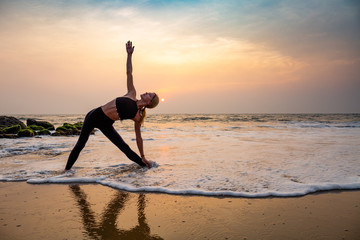 Middle age woman in black doing yoga on sand beach in India