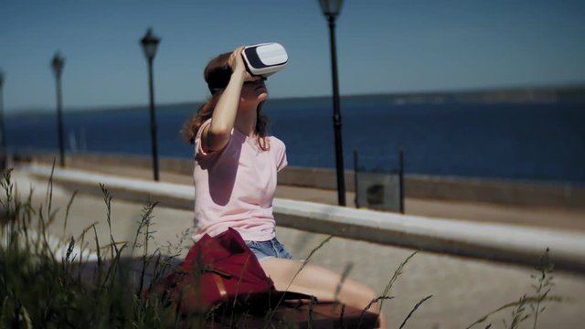 Young woman uses head-mounted display in the park. Playing game using VR-helmet for smart phones. Happy