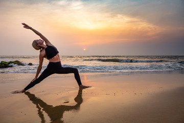 Fototapeta na wymiar Middle age woman in black doing yoga on sand beach in India
