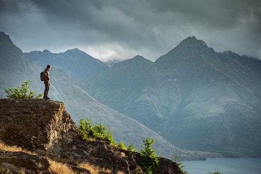 Young male photographer looking at mountain scenery during golden hour sunset in Queenstown, South Island, New Zealand. Travel and photography concept