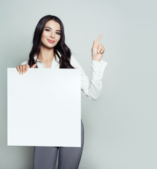 Friendly young woman with empty white blank paper banner background pointing her finger up. Girl...