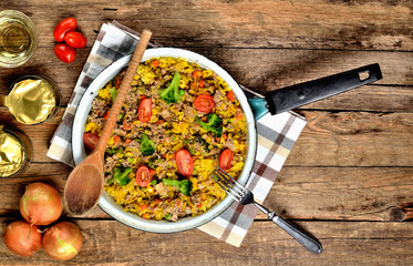 View from above of tuna risotto with vegetables, tomatoes, broccoli and parsley in the old pan, onions, cans and oil in the background