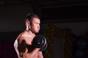 Fototapeta na wymiar Muscular young man lifting weights on dark background