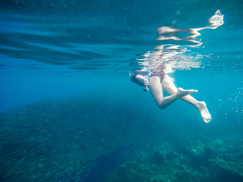 Woman swimming underwater in coral reef with sardine school. Summer vacation tourist with action camera.