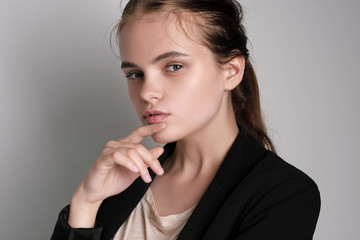 Portrait on shoulders of beautiful young girl with red brown hair in black jacket on gray background in studio.