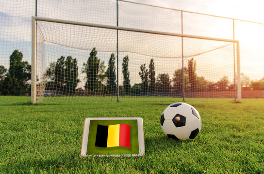 Soccer ball in front of empty goal and flag of Belgium on digital tablet on the grass