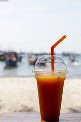 Mango smoothie cocktail with straw on white sand beach. Mango shake in plastic cup Cocktail on sunny seaside.