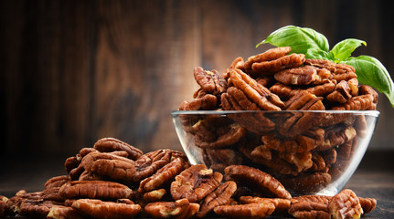 Bowl with pecan nuts on wooden table.