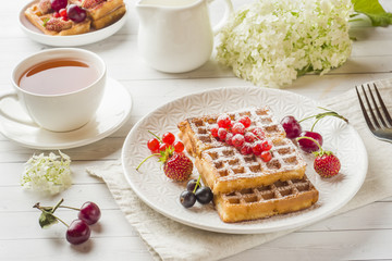Homemade waffles with summer berries on a plate. A Cup of tea on a light table. Selective focus