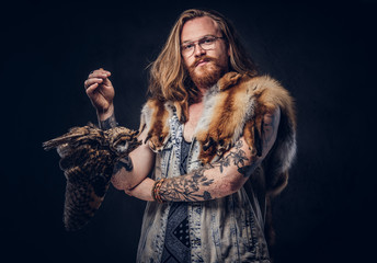 Portrait of a tattoed redhead hipster male with long luxuriant hair and full beard dressed in a...