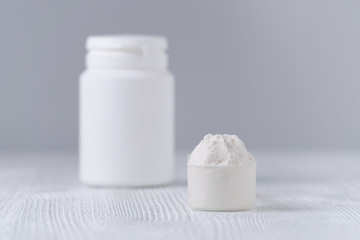 a scoop with white powder closeup and a jar on gray background