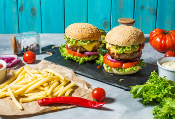 Two beef burgers, fries potatoes and cucumber on concrete table