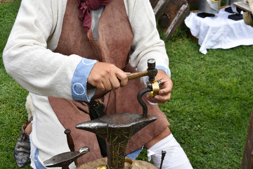 Craftsman coppersmith in medieval garment with hammer and anvil forges a copper bracelet - historical reconstruction, Mezdra, Bulgaria