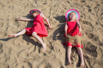children have fun on the sand on the beach, lying on the sand in red dresses and hats