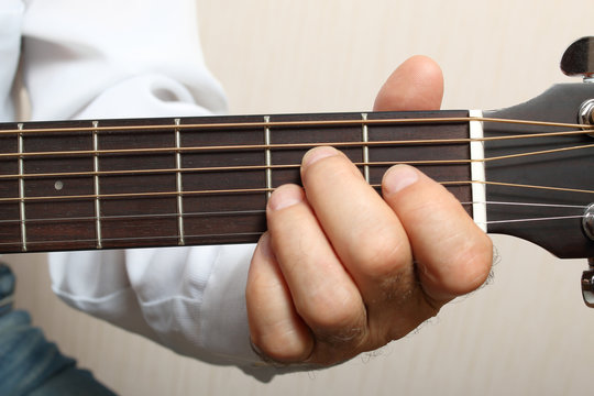 The musician in a white shirt playing acoustic guitar. Left hand on guitar neck