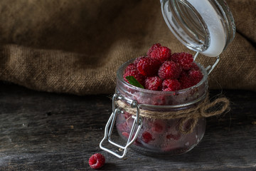 Raspberry in a glass jar on dark wooden background. Raspberry background. Healthy food concept. Fresh organic berries