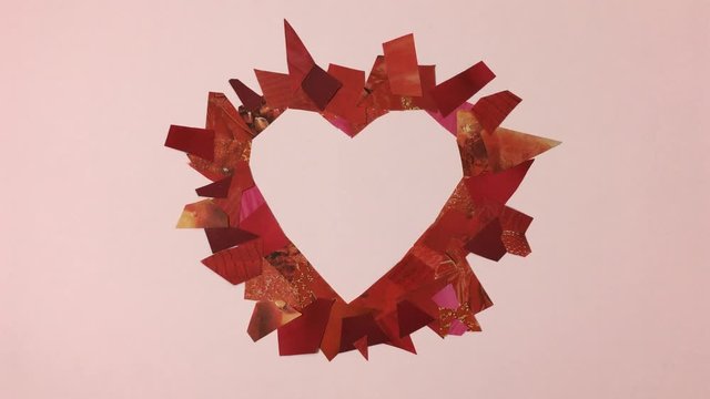 Corazon hecho de recortes de papel se deshace por el viento, sobre fondo rosa.