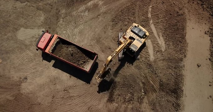 Aerial footageof excavator pours sand into the truck. On the construction site top view. Shooting from the drone/