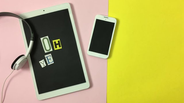Tablet, auriculares y telefono sobre fondo rosa y amarillo, aparece frase &ldquo;oh yeah&rdquo;.