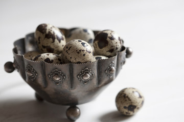 Closeup of quail eggs in a silver pot on white background; selective focus.