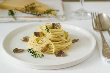 Pasta with creamy cheese sauce and truffle on a light plate, served with cheese and wine.