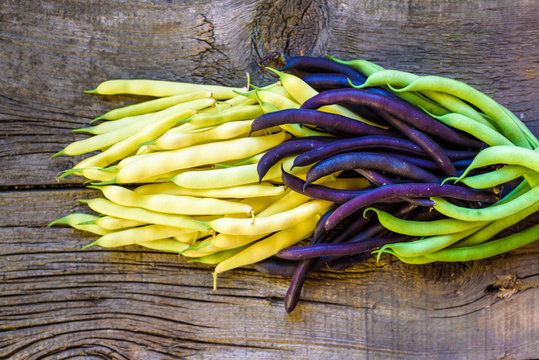 Collection of green, yellow and purple bush beans, opened green peas on wooden background