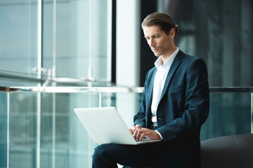 Young handsome man working in the office of mobile network company, adapting tariff plans to users need. Consultant providing service online with notebook. Business running through mobile systems. 