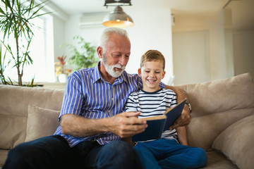 Grandfather With Grandson Reading Together On Sofa - obrazy, fototapety, plakaty