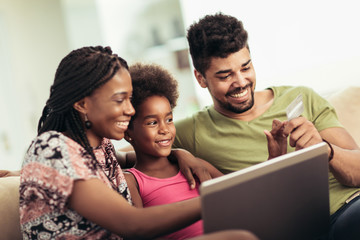 Cute little Afro-American girl and her beautiful young parents using a laptop and doing shopping...
