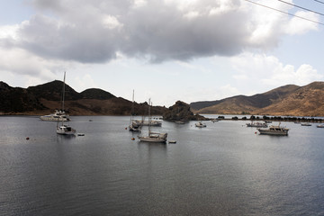 A view of a cloudy beach with yachts, boats and rocks in the island of Patmos, Greece in summertime