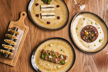 Table with food top view. Delicious luxury food table with slice of brie cheese, Smorrebrod, Danish open sandwich, labneh karri, and Beef tartare with egg yolk pistachios, truffle oil on wooden table