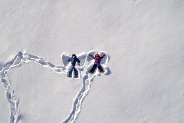Top angle view of kids lying on snow and making snow angel shape