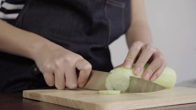 Close up of chief woman making salad healthy food and chopping cucumber on cutting board.