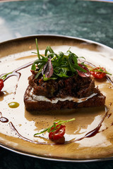 Bruschetta with lamb beef. Open sandwich with Dark rye bread, dried cherry tomatoes, rosemary, olives and arugula on plate at luxury restaurant table, top view. Delicious snack food 