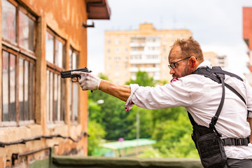 man dressed in a bulletproof vest, a shirt in his blood, pursues a victim with a gun Action Movie Style